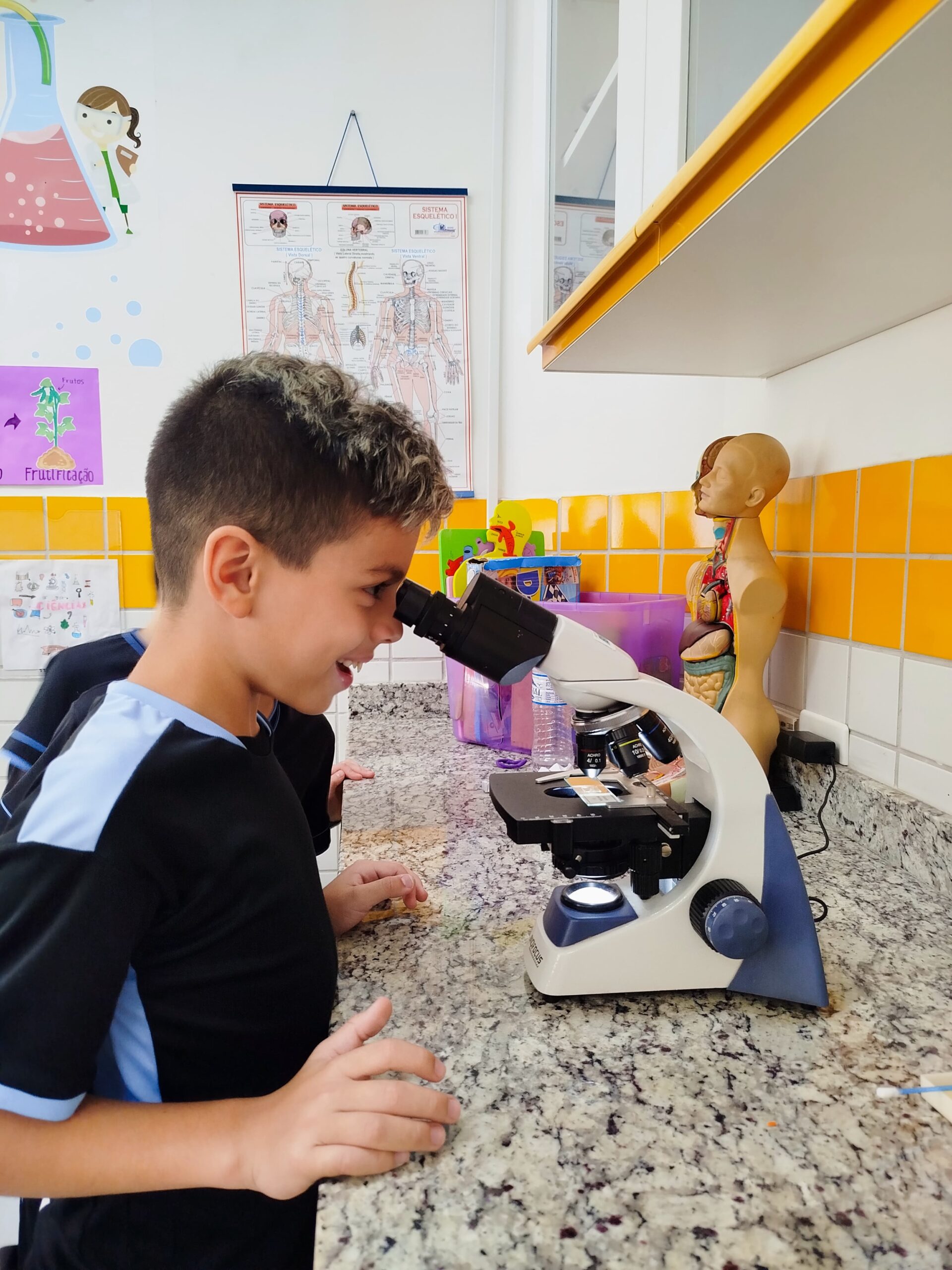 Aluno do 4º ano observa amostra sobre poluição em microscópio durante aula prática