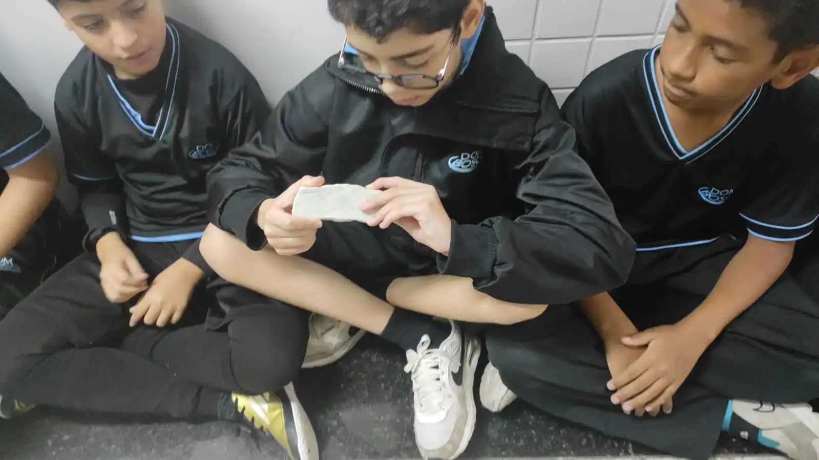 Grupo de alunos do 6º ano manuseia diferentes rochas em sala de aula.