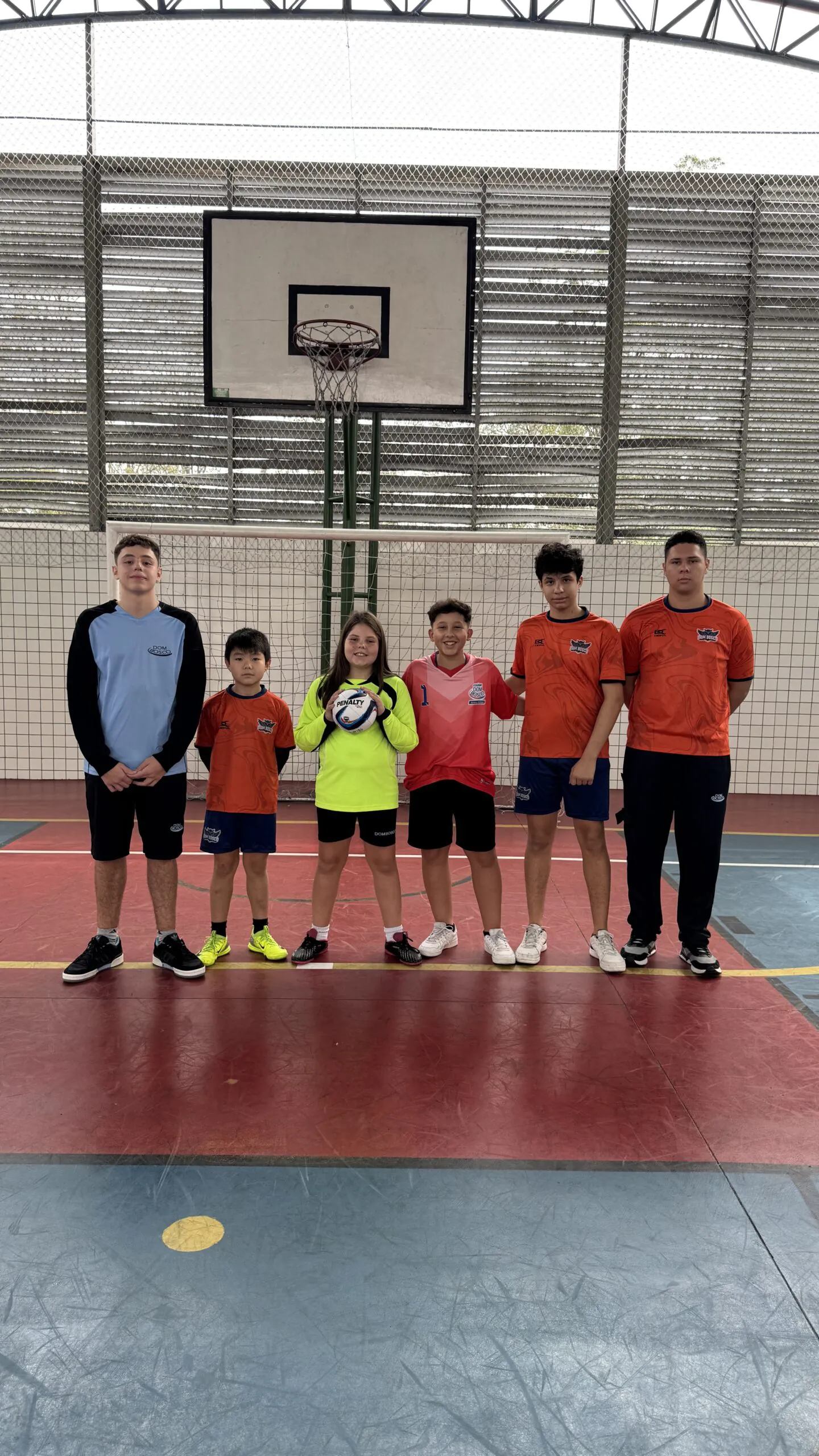 Alunos do Colégio Dom Bosco em quadra esportiva, uniformizados e sorridentes, celebrando o Dia do Goleiro com bola de futebol, destacando a importância do esporte na educação