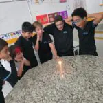 Alunos do 5º ano vivenciam uma aula prática no laboratório com a experiência da vela e da água, aprendendo sobre ar, pressão e ciência de forma lúdica
